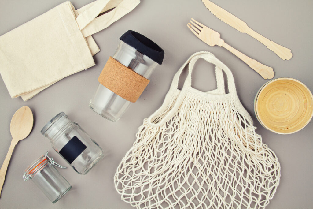 A collection of zero-waste lifestyle items, including a cotton tote bag, reusable glass containers, bamboo utensils, and a wooden bowl, symbolizing eco-friendly waste reduction and sustainable living practices.